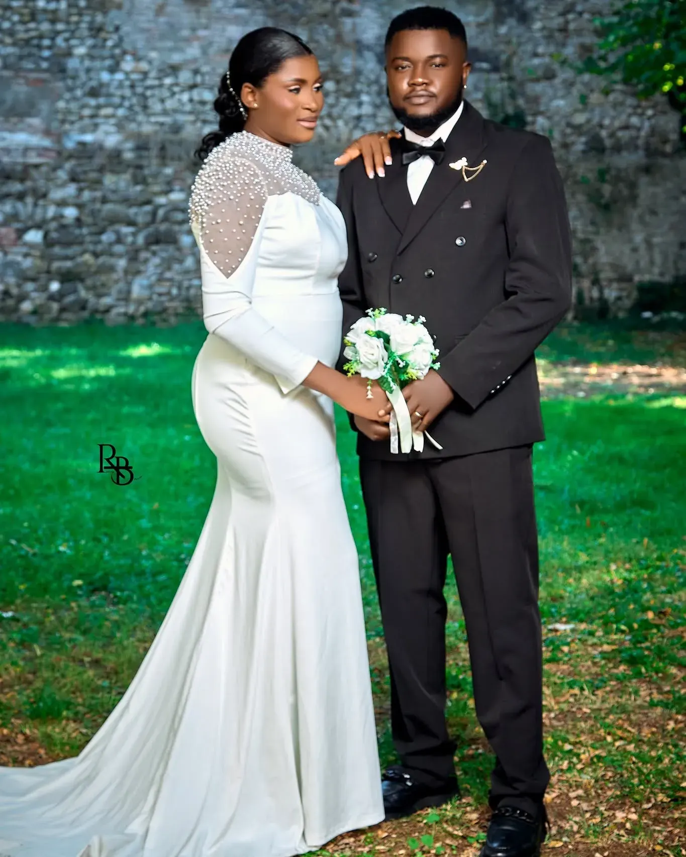 Bride and groom stand close outdoors while she holds a white bouquet.