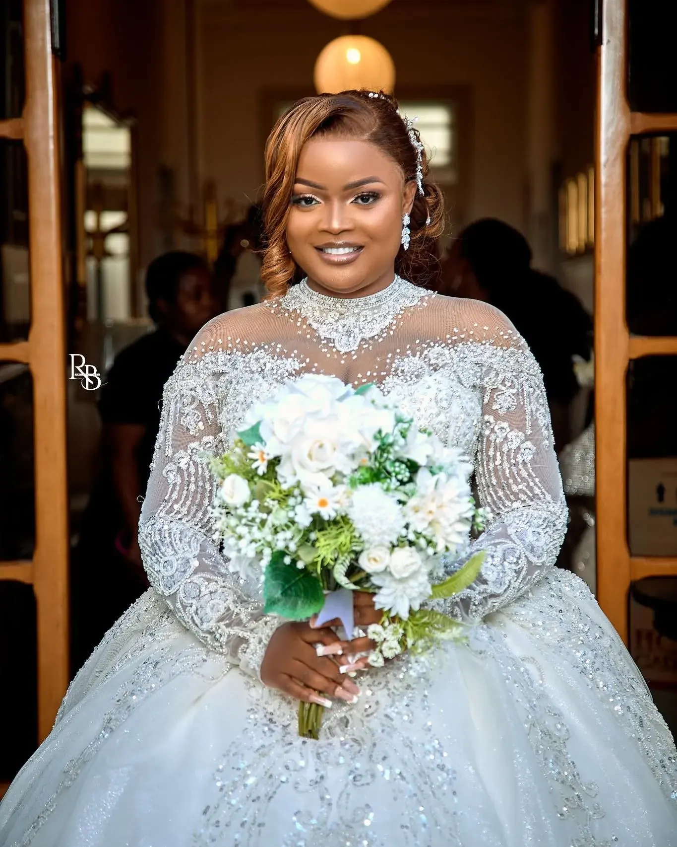 Bride smiles while holding a white and green bouquet in her gown.