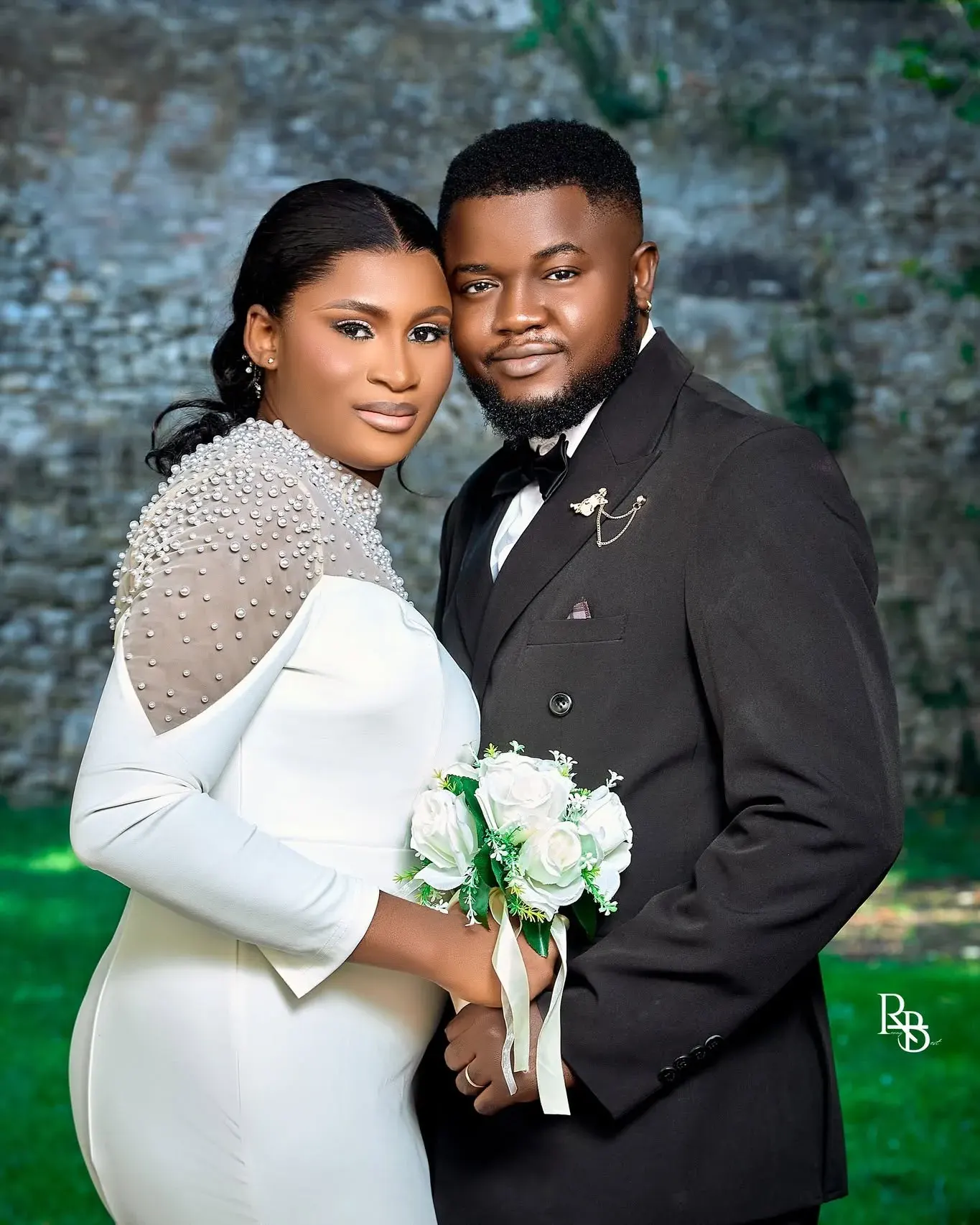 Bride and groom lean together smiling against a softly textured outdoor background.