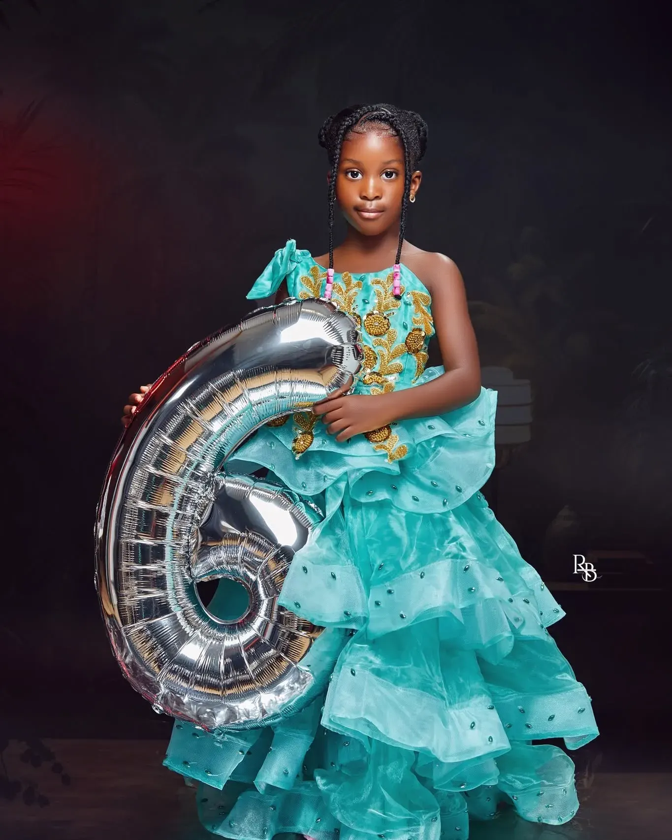 Girl in a turquoise dress holds a large silver number six balloon.