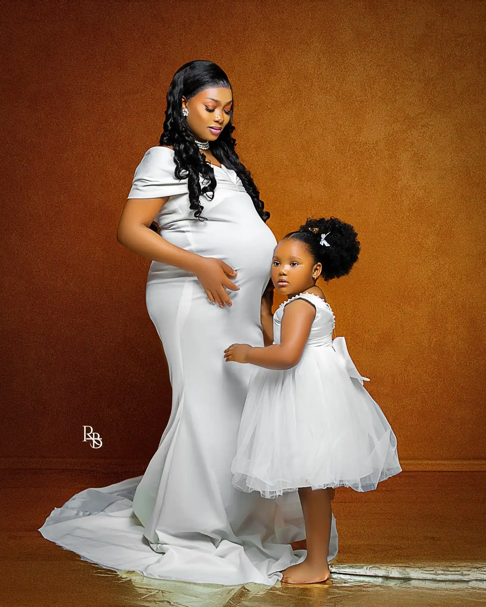 Pregnant woman in white stands beside a young girl in a matching dress.