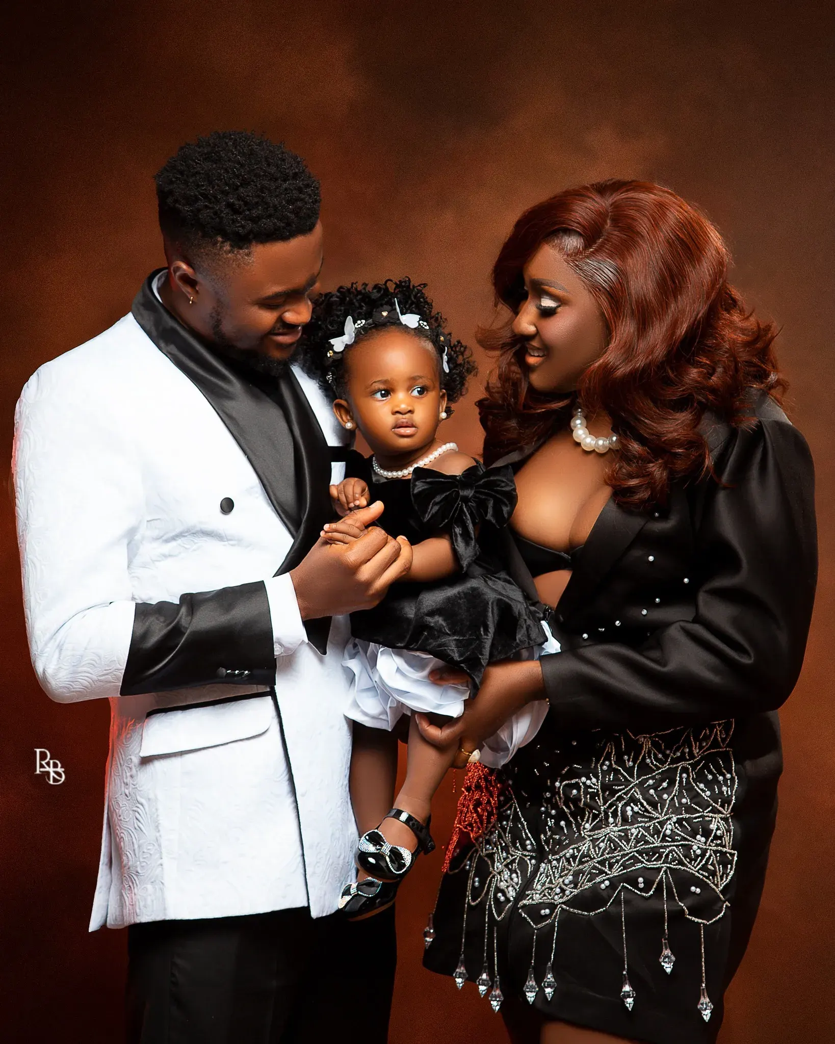 Two adults lean toward a young girl while posing in formal clothing.