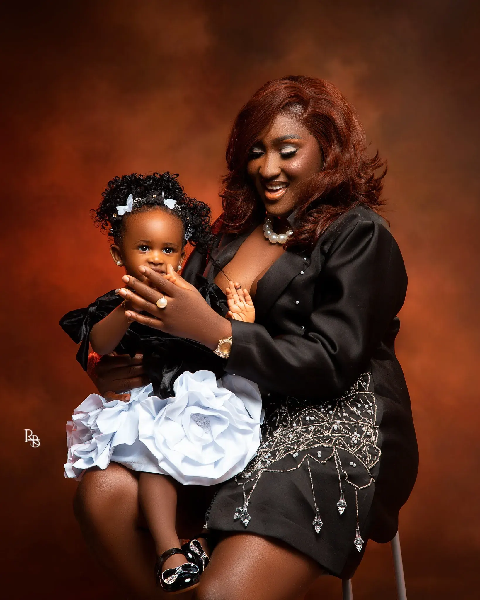 Woman in black holds a young girl on her lap while smiling.